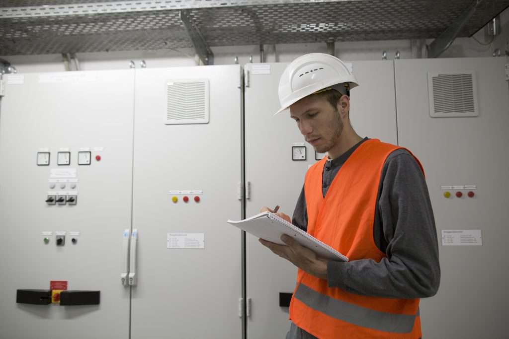 Young male electrician reading paperwork in technical room